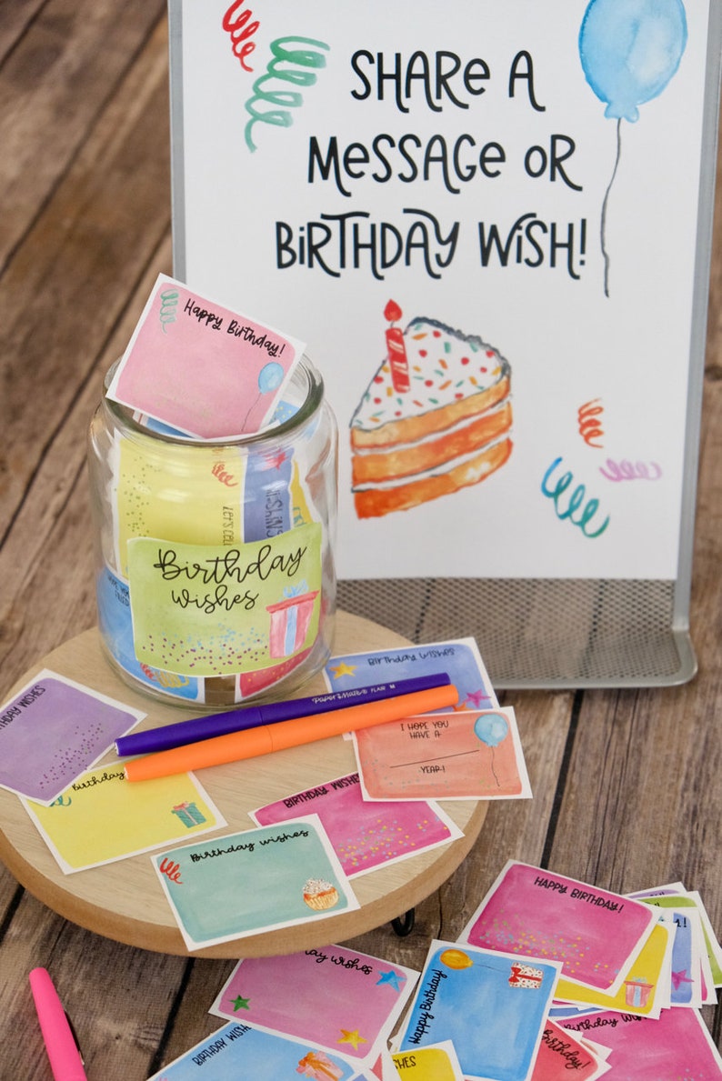 May include: A glass jar filled with colorful cards that say "Birthday Wishes" on them. The jar is surrounded by more cards with birthday wishes and a sign that says "Share a message or birthday wish!"