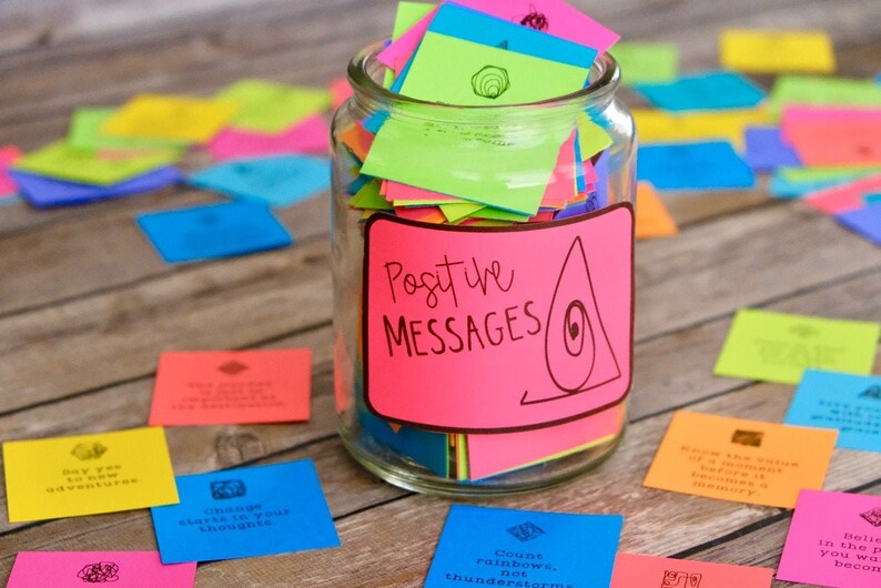 May include: A glass jar filled with colorful sticky notes, labeled "Positive Messages". The jar is surrounded by more sticky notes on a wooden surface.