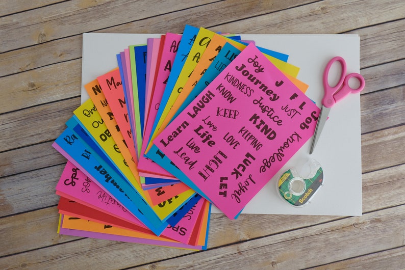 Peut inclure: Un ensemble de cartes en papier color&eacute;es avec des mots positifs imprim&eacute;s dessus, tels que "Joie", "Bienveillant", "Apprendre", "Amour" et "Vie". Les cartes sont dispos&eacute;es en &eacute;ventail sur une surface blanche. On voit &eacute;galement des ciseaux, du ruban adh&eacute;sif et une feuille de papier blanche sur l'image.