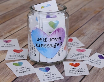 May include: A glass jar filled with colorful cards that have self-love messages written on them. The jar is labeled "self-love messages".