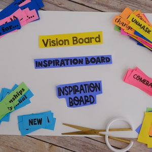 Peut inclure: Un tableau blanc avec les mots "Vision Board" et "Inspiration Board" &eacute;crits en noir. Il y a des bandes de papier color&eacute;es avec des mots &eacute;crits dessus, comme "Saving for...", "Comeback", "Love Your Life", et "Unmask Your Inner Hero". Il y a aussi des ciseaux sur le tableau.