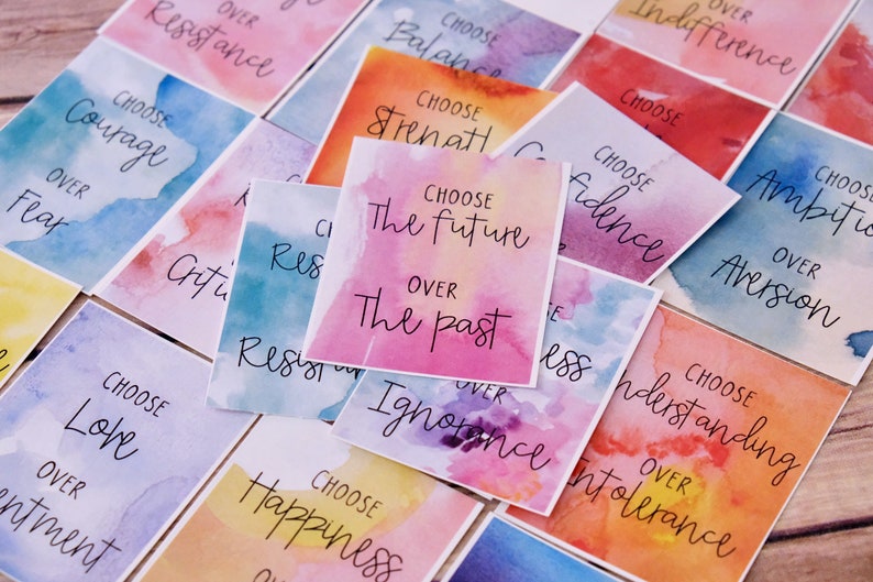 May include: A set of colourful watercolour cards with inspirational messages. Each card features a different colour scheme and a handwritten message encouraging the viewer to choose one thing over another. For example, one card says "Choose the future over the past".