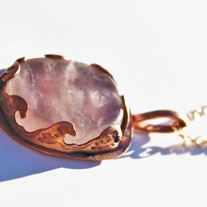 May include: A delicate copper pendant necklace with a light pink, cloudy agate stone set in a detailed, ornate copper frame.