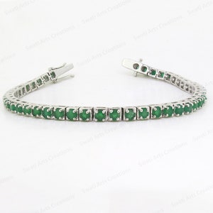 Puede incluir: Un brazalete de tenis de plata con una fila de piedras preciosas de color verde esmeralda.
