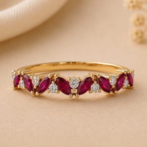 May include: A gold ring with alternating marquise-cut rubies and round diamonds. The gemstones are set in a repeating pattern around the band. The ring is displayed on a neutral background, with soft lighting.