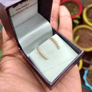 May include: A pair of gold earrings with a row of small diamonds set in a curved bar design. The earrings are in a small, red velvet box.