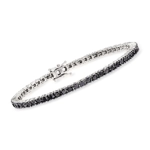 May include: A silver tennis bracelet with a row of black gemstones. The bracelet has a secure clasp and is displayed against a white background. The gemstones are evenly spaced and add a touch of elegance.