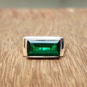 May include: A silver ring with a rectangular emerald green gemstone.