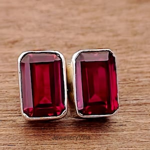 May include: A pair of silver earrings with red rectangular gemstones. The earrings have a simple design and are perfect for everyday wear.