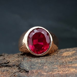 May include: A gold ring with a large, round, red gemstone.