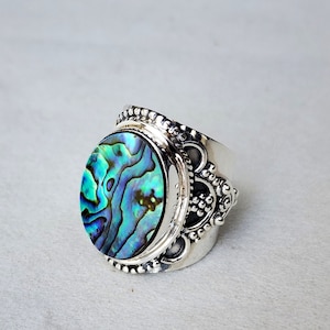 May include: A silver ring with an oval abalone shell inlay. The ring has a wide band with a decorative design.