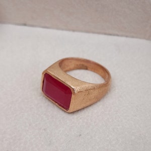 Op de afbeelding: Een gouden ring met een grote, rechthoekige, rode edelsteen.