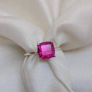 Pode incluir: Um anel de prata com uma grande pedra preciosa rosa de forma quadrada.