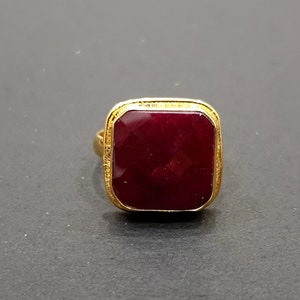 May include: A gold ring with a square-shaped, dark red gemstone.