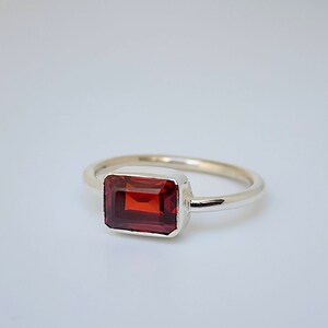 May include: A silver ring with a red rectangular gemstone.