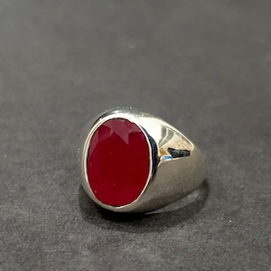 May include: A silver ring with a large, oval-shaped, red gemstone.