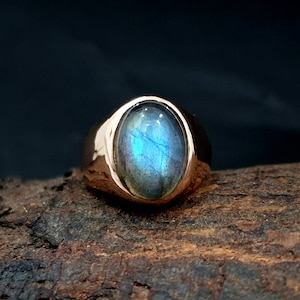 Puede incluir: Un anillo de oro con una gran piedra ovalada de labradorita azul.