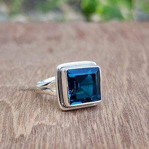 Puede incluir: Un anillo de plata con una gran piedra de topacio azul cuadrada. El anillo tiene un diseño simple y elegante.