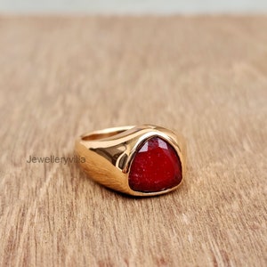 May include: A gold ring with a large, triangular, red gemstone.
