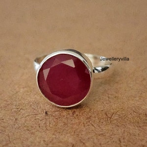 May include: A silver ring featuring a large, round, faceted, red gemstone.