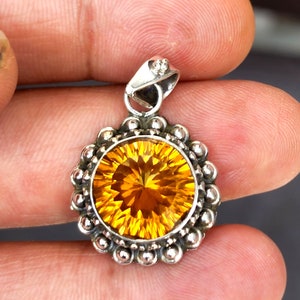May include: A silver pendant featuring a round, faceted, orange gemstone set in a silver bezel. The pendant is encircled by a silver beaded border.
