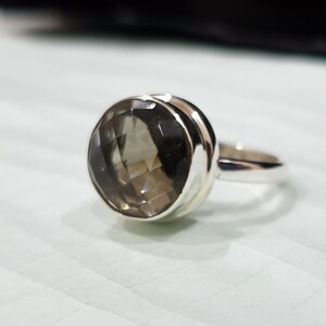 May include: A silver ring featuring a round, faceted, smoky quartz gemstone.