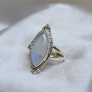 May include: A silver ring with a marquise-shaped moonstone set in a detailed silver bezel. The ring has a delicate, feminine design.