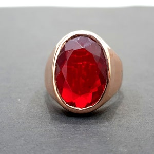 May include: A red gemstone ring with a gold band. The ring has a large, oval-shaped gemstone.