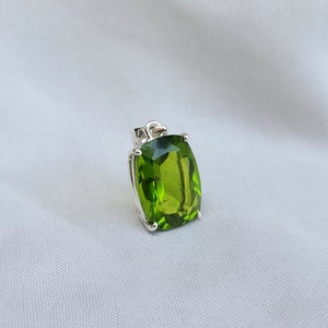 May include: A silver pendant with a large, green, faceted gemstone. The gemstone is set in a silver bezel and has a rectangular shape.