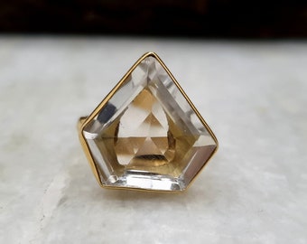 May include: A gold ring with a clear, faceted gemstone in a geometric shape.