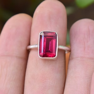 Op de afbeelding: Een zilveren ring met een grote, rechthoekige, donkerrode edelsteen.