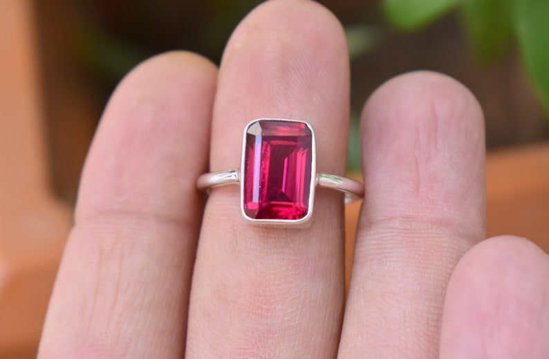 Op de afbeelding: Een zilveren ring met een grote, rechthoekige, donkerrode edelsteen.