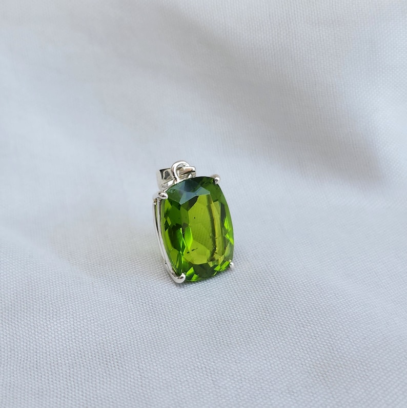 May include: A silver pendant with a large, green, faceted gemstone. The gemstone is set in a silver bezel and has a rectangular shape.