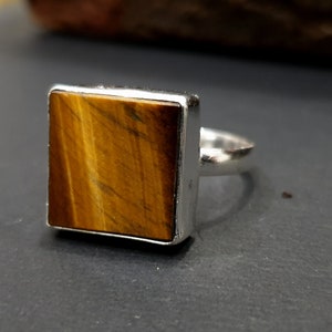May include: A silver ring with a square-shaped tiger's eye gemstone.