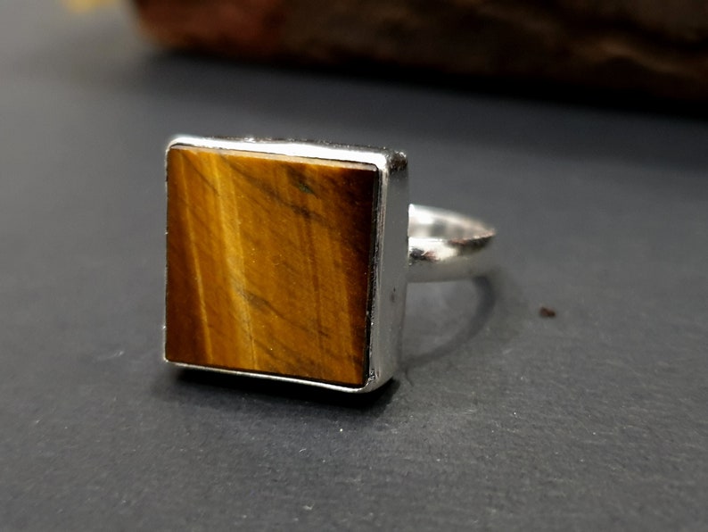May include: A silver ring with a square-shaped tiger's eye gemstone.