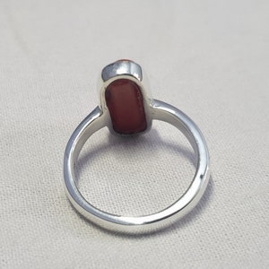 May include: A silver ring with a red gemstone. The ring is shown from the back, so the setting is visible.