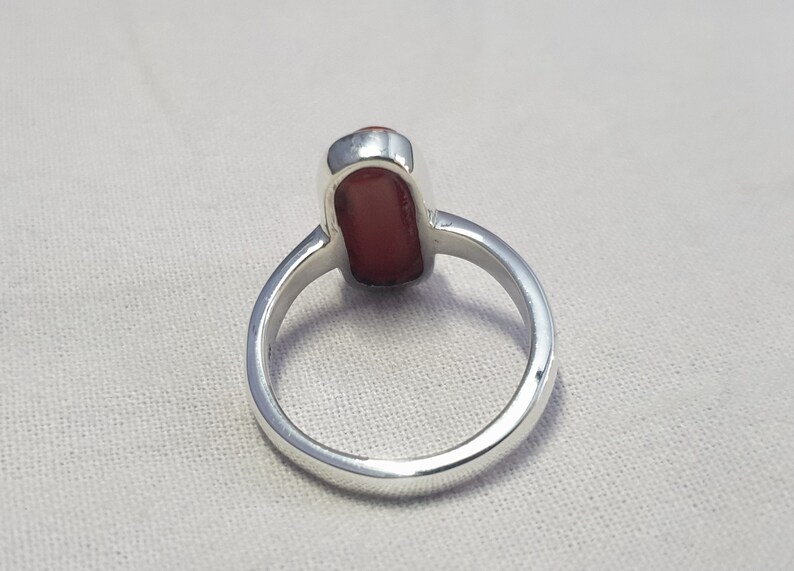 May include: A silver ring with a red gemstone. The ring is shown from the back, so the setting is visible.