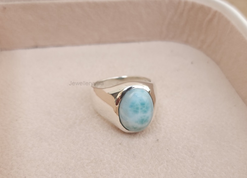 K&ouml;nnte beinhalten: Ein silberner Ring mit einem ovalen, hellblauen Edelstein. Der Edelstein hat ein wirbelndes Muster.