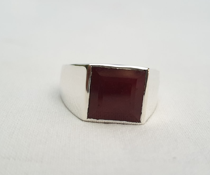 Peut inclure: Une bague en argent avec une pierre carr&eacute;e rouge fonc&eacute;.