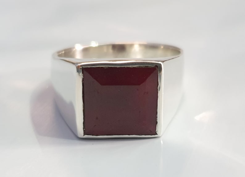 Peut inclure: Une bague en argent avec une pierre carr&eacute;e rouge fonc&eacute;.