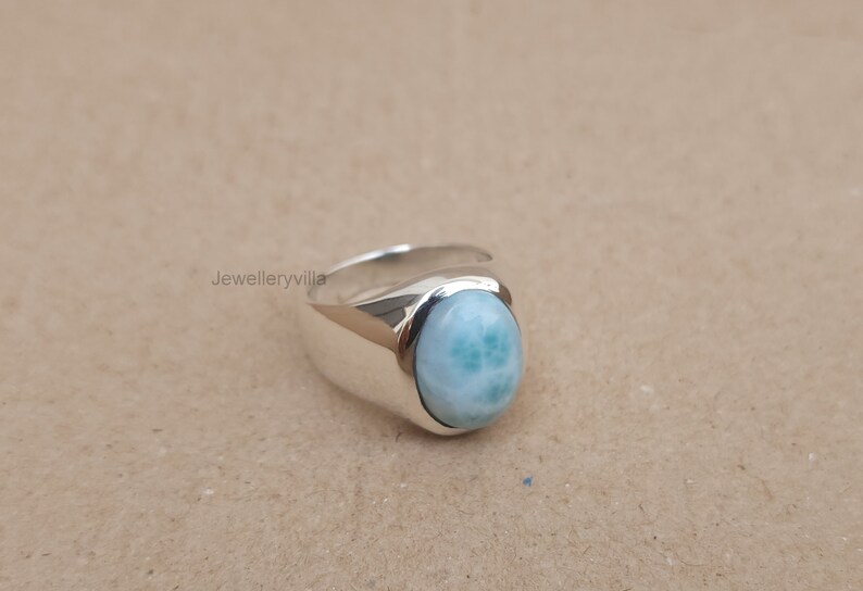 K&ouml;nnte beinhalten: Ein silberner Ring mit einem ovalen, blau-gr&uuml;nen Edelstein. Der Ring hat ein breites Band.