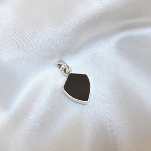 May include: A silver pendant in the shape of a shield with a black onyx stone.