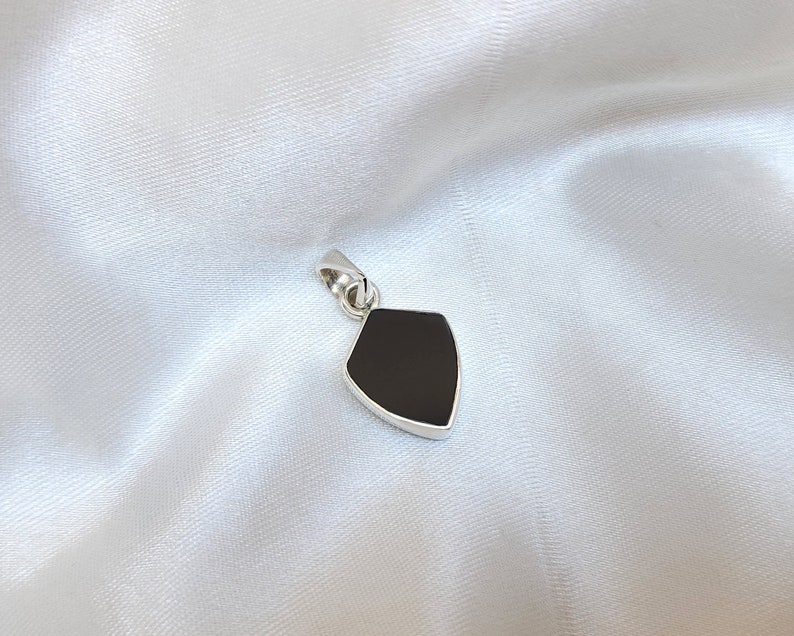 May include: A silver pendant in the shape of a shield with a black onyx stone.