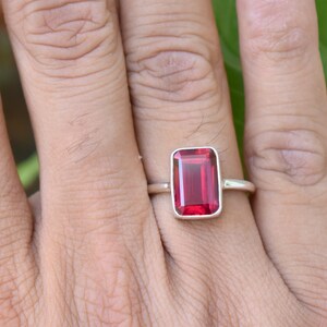 Op de afbeelding: Een zilveren ring met een rechthoekige rode edelsteen. De ring wordt gedragen aan een vinger.