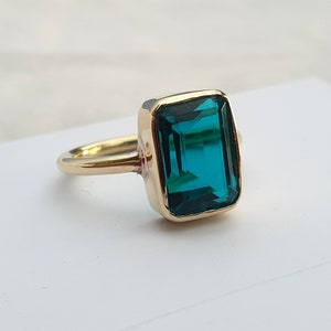 May include: A gold ring with a large, emerald green gemstone set in a square shape.