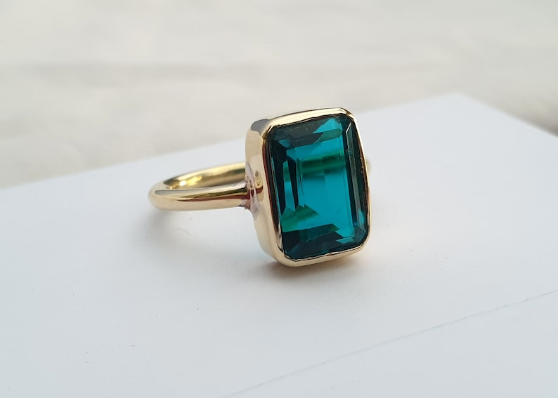 May include: A gold ring with a large, emerald green gemstone set in a square shape.