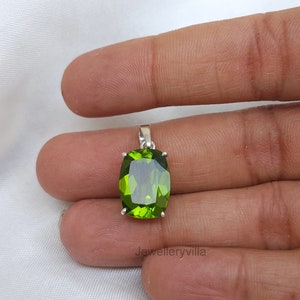 May include: A green gemstone pendant with a silver setting. The gemstone is oval shaped and has a faceted cut. The pendant is hanging from a silver chain.