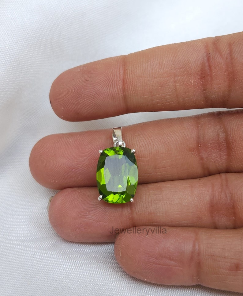 May include: A green gemstone pendant with a silver setting. The gemstone is oval shaped and has a faceted cut. The pendant is hanging from a silver chain.