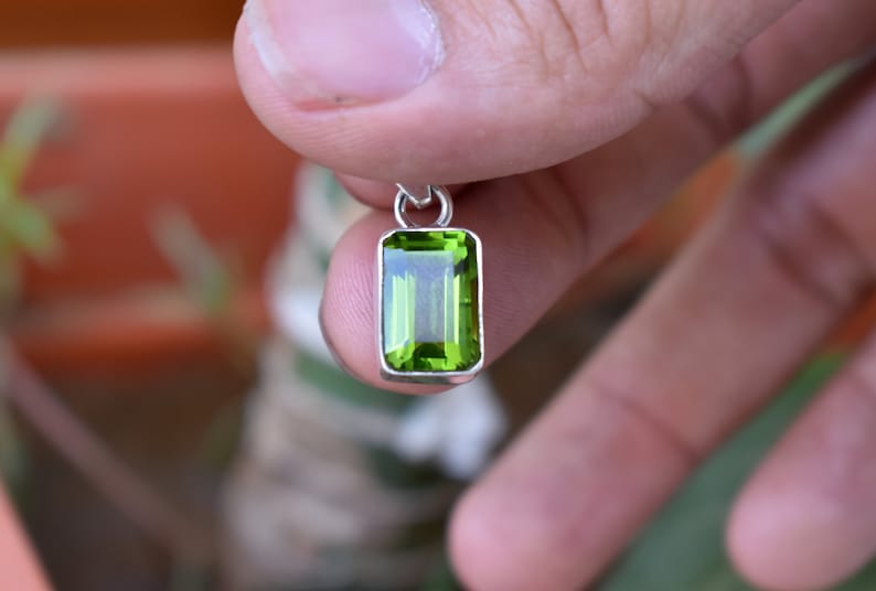 Puede incluir: Un colgante de plata con una piedra preciosa verde. La piedra preciosa est&aacute; tallada en forma de esmeralda.