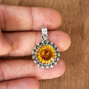 May include: A silver pendant featuring a round, faceted, orange gemstone set in a silver bezel with a beaded border.